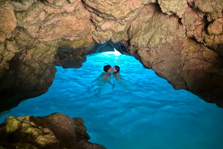 Couple swimming in a cave with blue water and rocky walls.