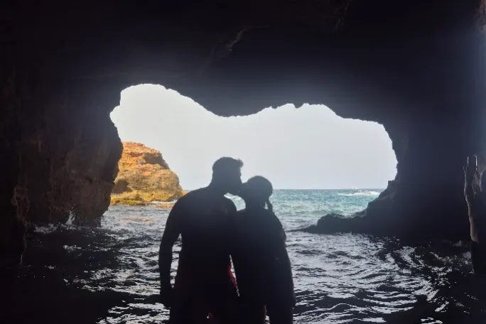 Silhouetted couple standing in a cave with an ocean view.