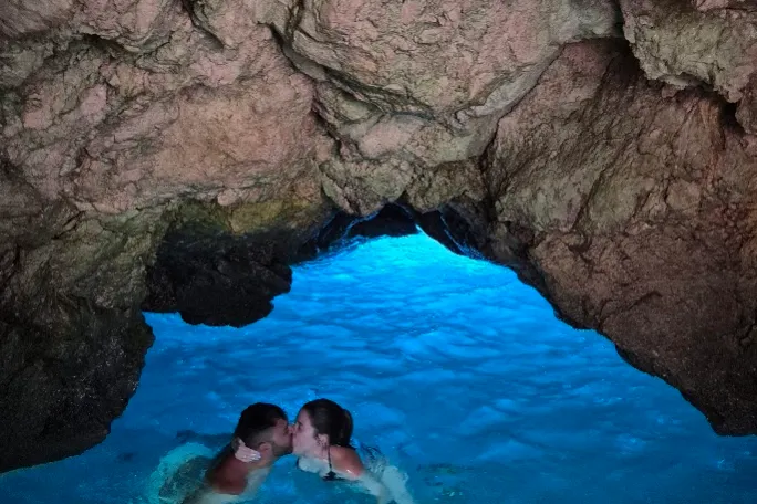 Two people kissing in a brightly lit cave pool with rocky walls.