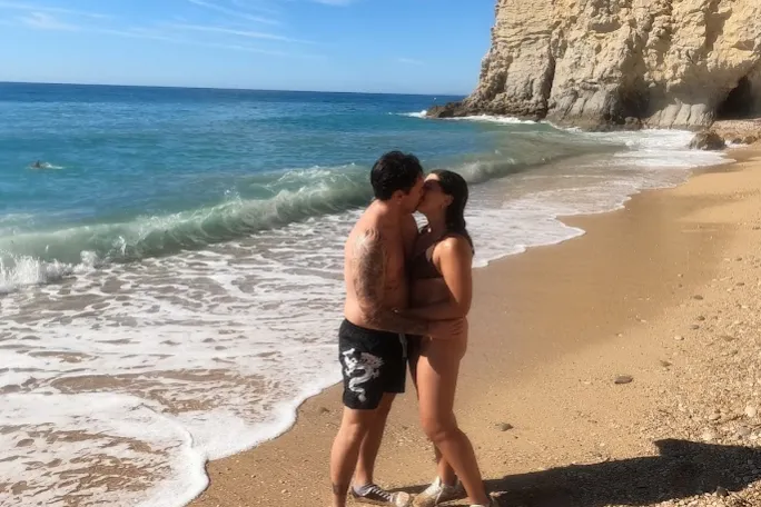 Couple kissing on a sandy beach with cliffs and blue ocean.
