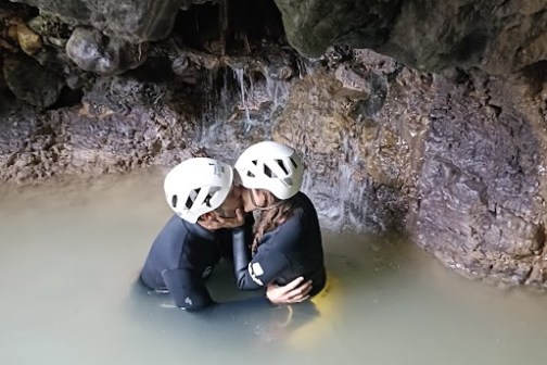 Two people in helmets kissing in a cave pool.