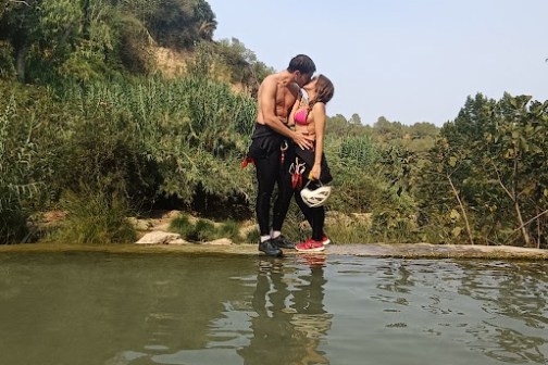 Couple kissing near a reflective water surface with greenery in the background.