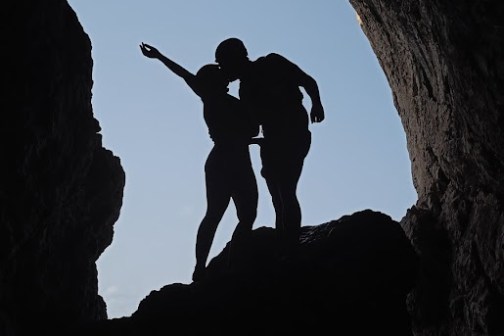 Silhouetted couple standing in a cave entrance, with one person raising an arm.