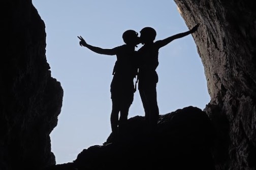 Two silhouettes embracing on a rock inside a cave entrance.