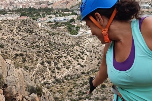 Two people in climbing gear on a rocky hillside with a city view behind.