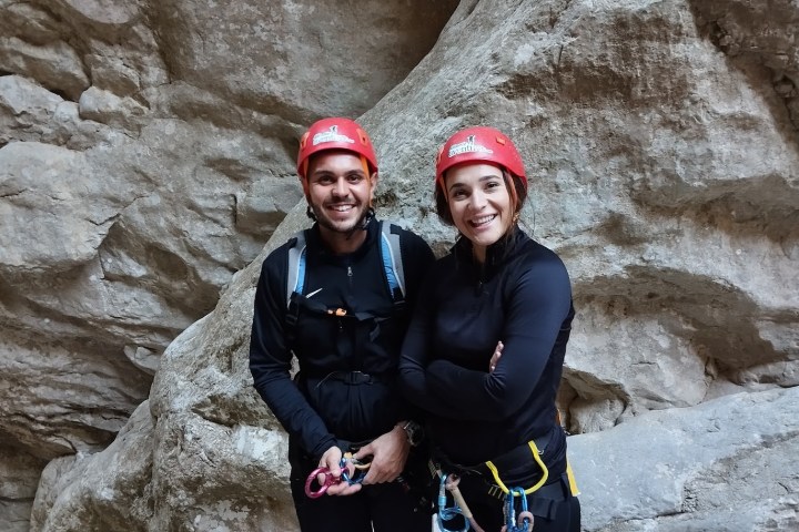 Two people in red helmets smiling, standing in a rocky area.