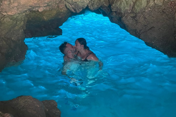 Couple kissing in bright blue water inside a rocky cave.