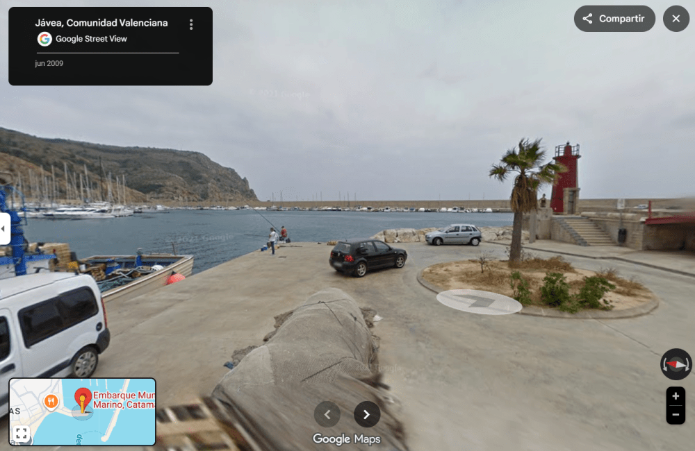 Coastal area with parked cars, palm tree, and red lighthouse near the sea, Javea, Comunidad Valenciana.
