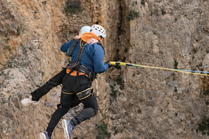 Two people in helmets and harnesses bungee jumping off a cliff.
