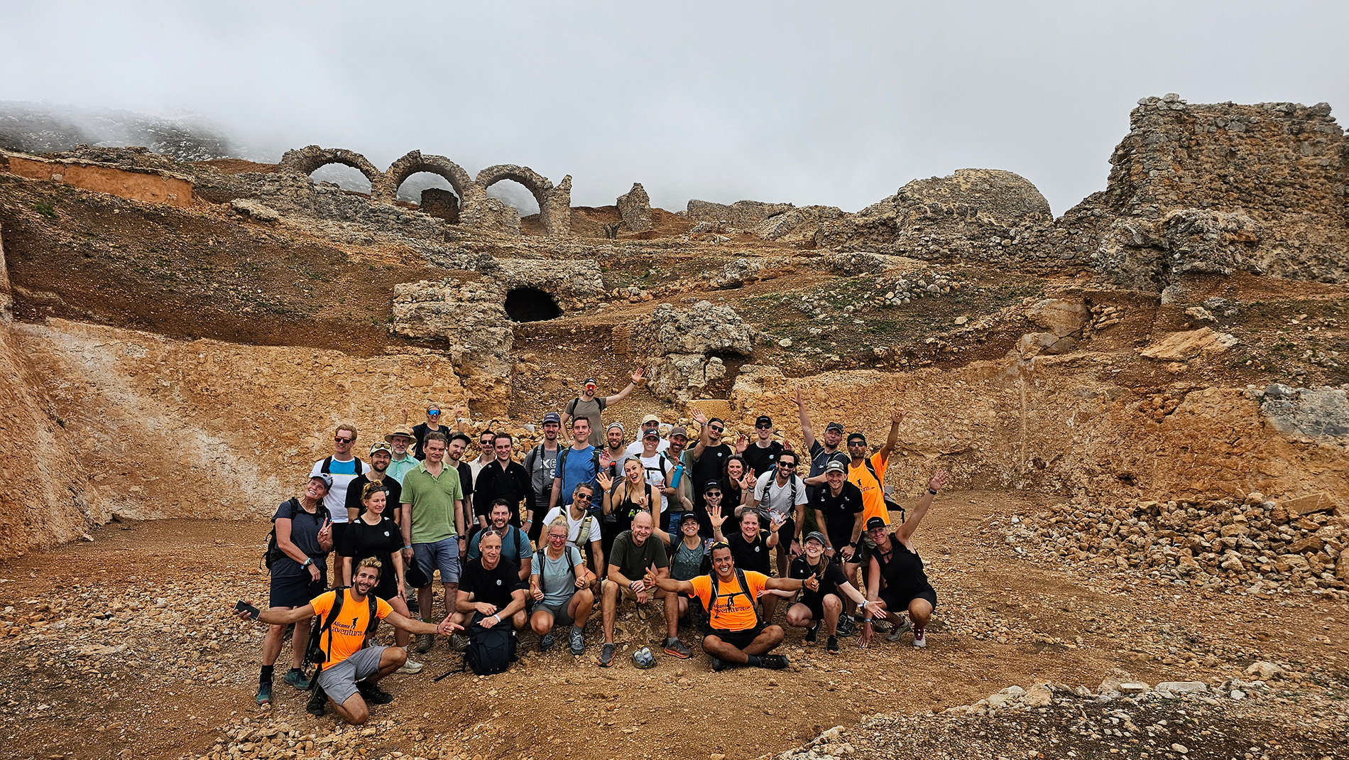 Group of people posing at ancient ruins site with arch structures.