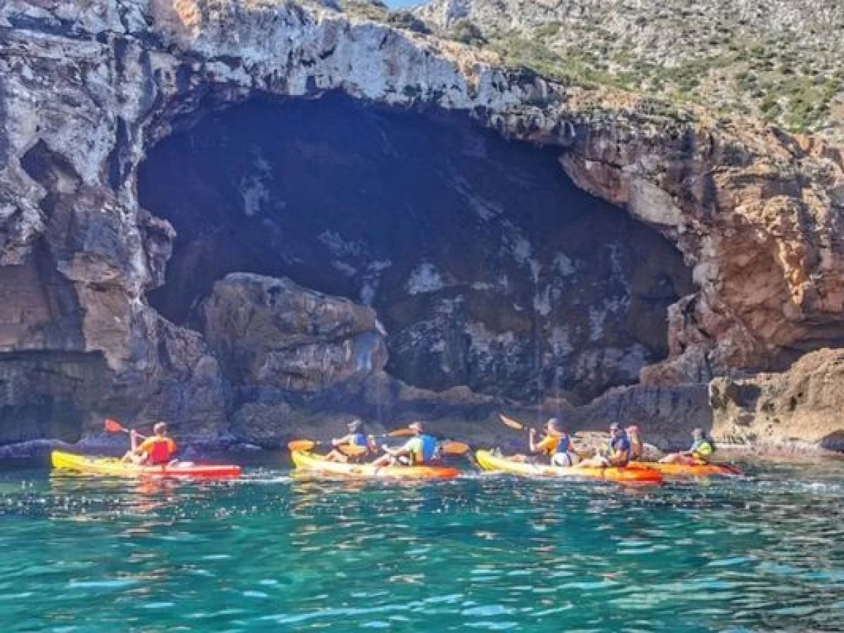 Grupo recorriendo la costa en kayak frente a una gran cueva marina con Alicante Aventura