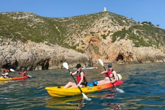 Dos participantes disfrutando de una ruta en kayak con la torre del Cabo de Sant Antoni al fondo