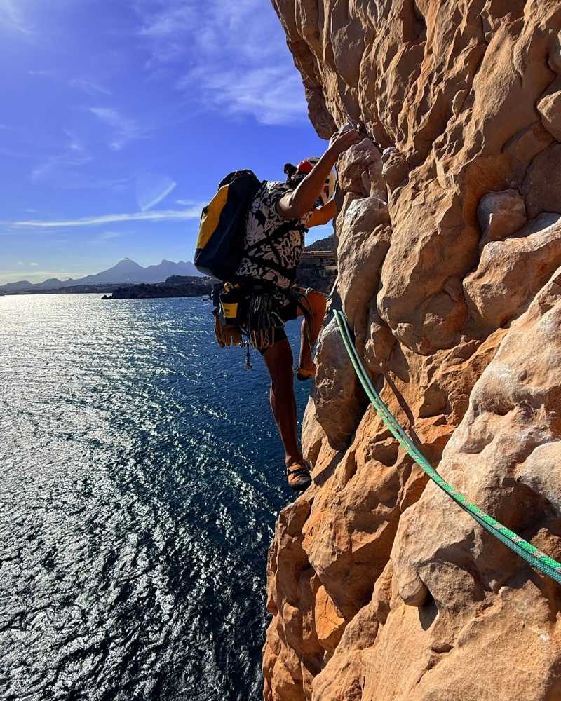 Escalador progresando por una pared vertical del Morro de Toix durante la ruta Magical Mystery Tour, sobre el mar Mediterráneo