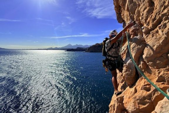 Escalador progresando por una pared del Morro de Toix con el mar Mediterráneo al fondo