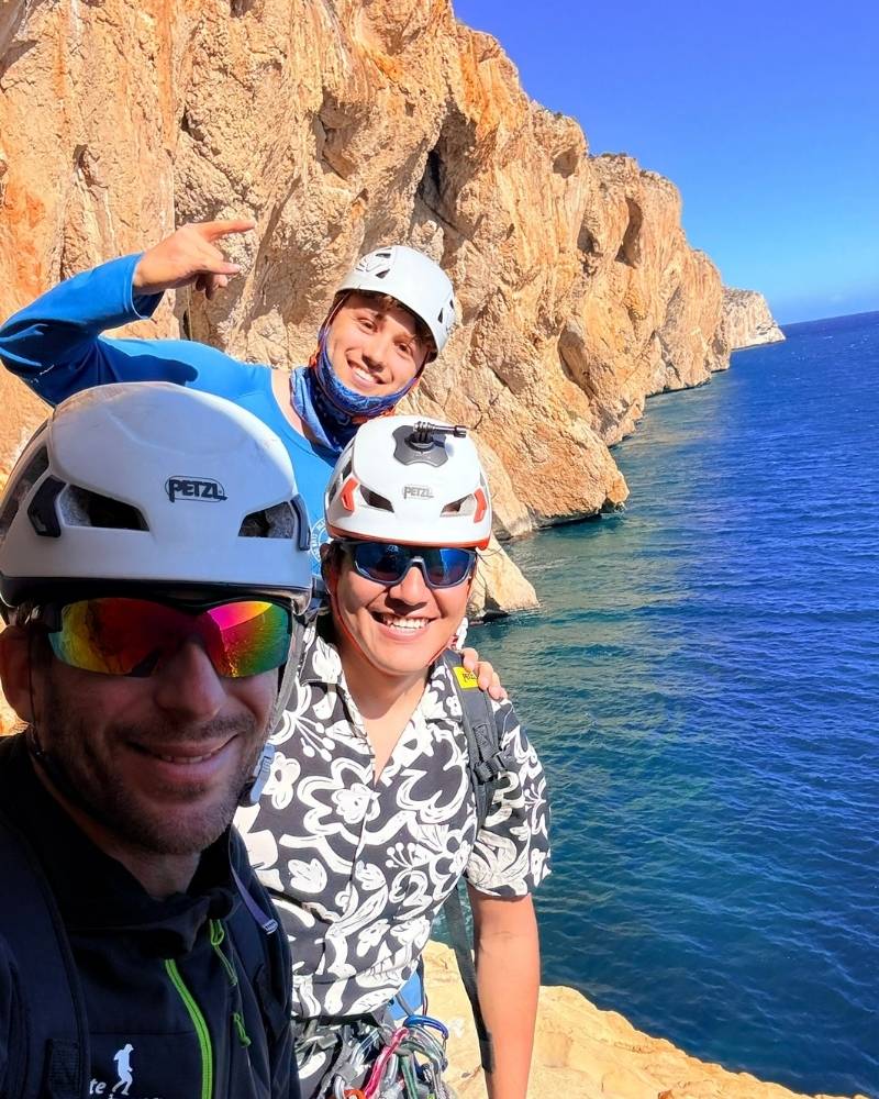 Toni y dos escaladores sonrientes durante la ruta Magical Mystery Tour en el Morro de Toix, con los acantilados y el Mediterráneo de fondo