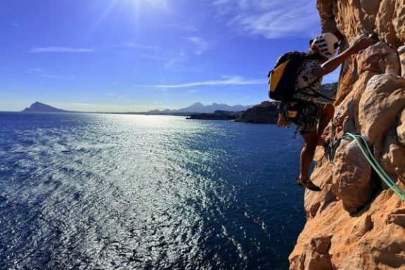 Escalador ascendiendo una pared vertical del Morro de Toix con vistas al Mediterráneo