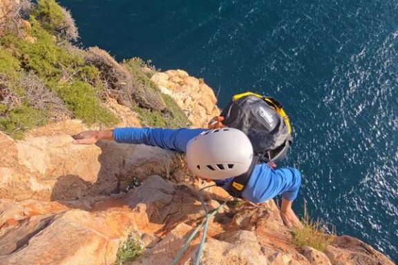 Escalador progresando por una pared de roca con el mar bajo el acantilado