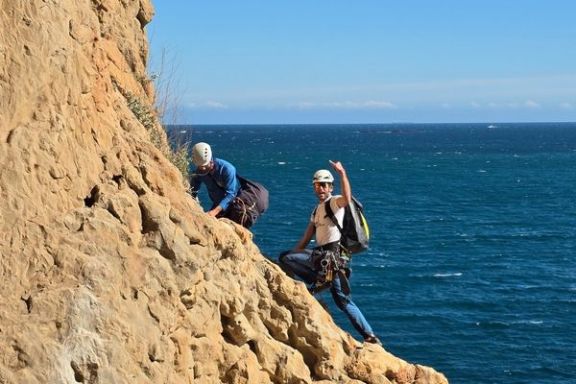 Dos escaladores avanzando por el acantilado del Morro de Toix con el Mediterráneo detrás